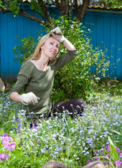 Young pretty woman looks after behind plants in the garden..