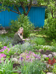 Young pretty woman looks after behind plants in the garden..