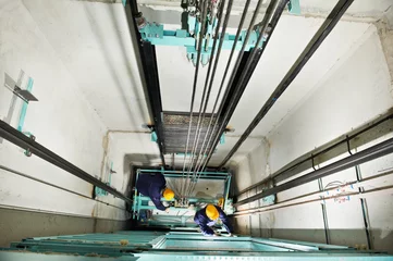 Fotobehang machinists adjusting lift in elevator hoistway © Kadmy