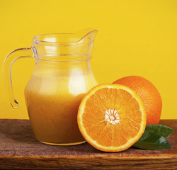 Orange juice in pitcher and oranges. Isolated on yellow