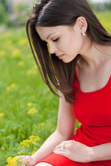 Naklejka na ściany i meble Young pretty woman in red dress sitting on green grass