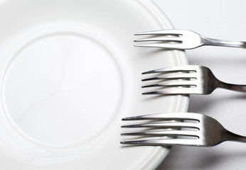 White plate, fork  on light background.
