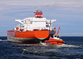 Tugboat towing a large cargo ship in port.