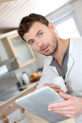 Young man using electronic tablet while drinking coffee