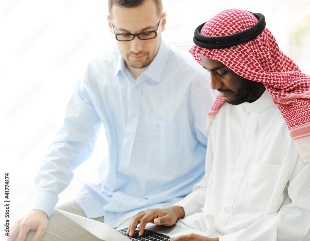 Wall mural arabic black and caucasian men working together on laptop