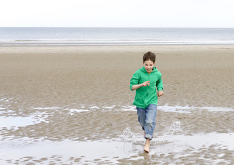 the boy in a green hoodie, running barefoot on the beach at low