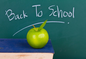 Back to school written on chalkboard with green apple and books