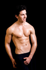 Fototapeta premium Smiling fit man flexing his muscles on black background