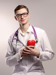 Male doctor with stethoscope holding heart on white background.