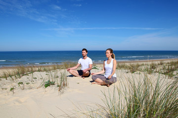 Couple doing yoga exercices on a sandy beach