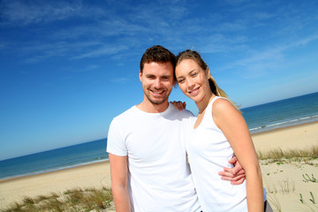 Smiling couple in fitness outfit standing on the beach