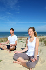 Couple doing yoga exercices on a sandy beach