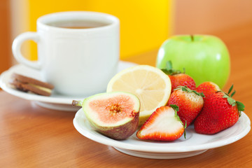 cup of tea,cookie,apple, lemon, fig and strawberries on a plate