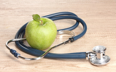Medical stethoscope and green apple on wooden background