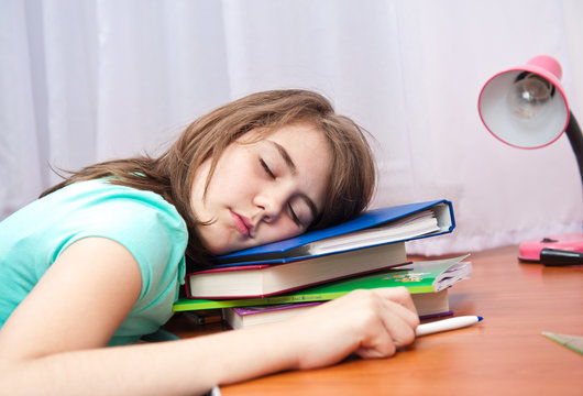 cute teenage girl sleeping on a stack of books at her desk