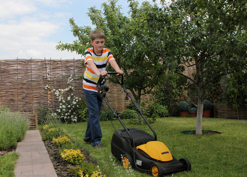 Teen boy mows the lawn mower electric