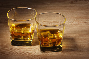 two glasses of scotch whiskey and ice on wooden table