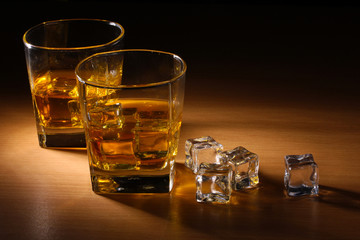 two glasses of scotch whiskey and ice on wooden table