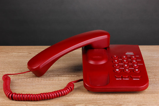 Red phone on wooden table on grey background