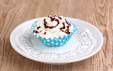 Creamy cupcake on saucer on wooden background