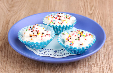 Creamy cupcakes on saucer on wooden background