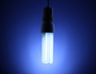 A lit energy saving light bulb on blue background