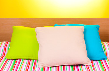 bright pillows on bed on yellow background