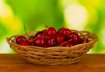cherry in wicker bowl on wooden table on green background