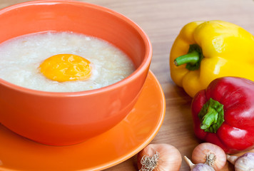Rice porridge with egg in orange bowl.