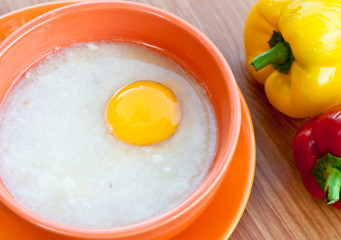 Rice porridge with egg in orange bowl.