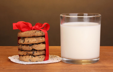 Glass of milk and cookies on wooden table on brown background