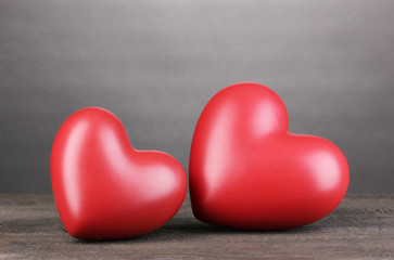 Two decorative red hearts on wooden table on grey background