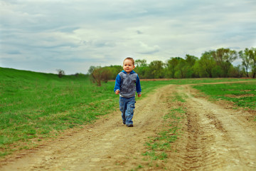 Naklejka na ściany i meble little baby boy walking country road on cloudy sky background