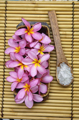 frangipani and salt in wooden spoon on mat