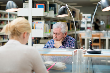 Senior man studying among young people in library