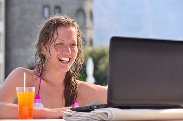woman is using laptop from swimming pool near the hotel