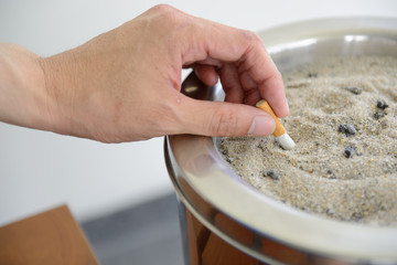 Male hand Stubbing Out Cigarette in sand ashtray bin