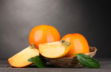 Appetizing persimmons in pad on wooden table on grey background