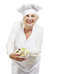senior woman cook holding a bowl with salad against a white back