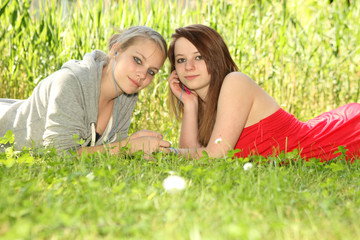 young teenager girls sharing music on a meadow