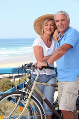 Mature couple with bikes by a beach - obrazy, fototapety, plakaty