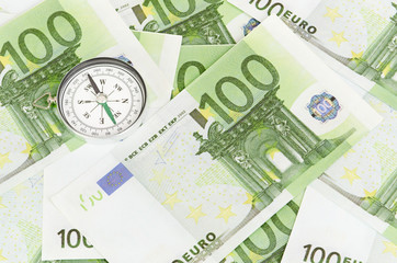 many euro bank notes and a compass lie side by side