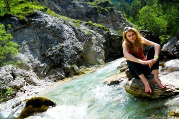 Fototapeta na wymiar Girl sits on a stone by clean river in the Austrian Alps