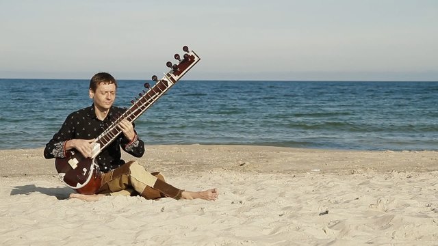 Man plays the sitar on the beach