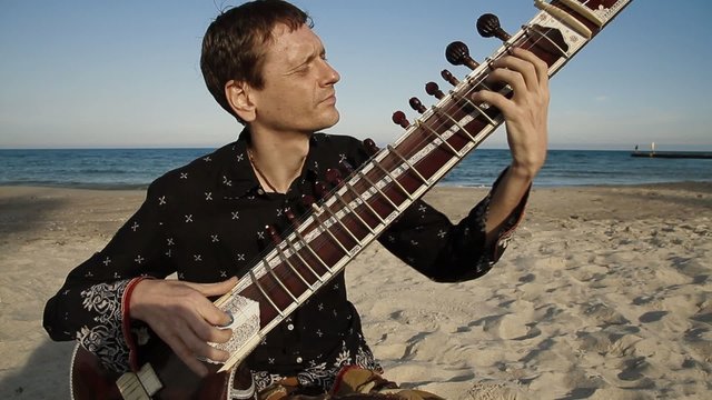 Man plays the sitar on the beach