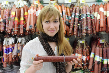 Smiling girl wearing scarf chooses sausage in large store