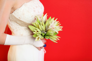 hands of young bride hold bouquet of lilies on red background