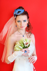 bride wearing white dress with blue mask in hairdo holds bouquet