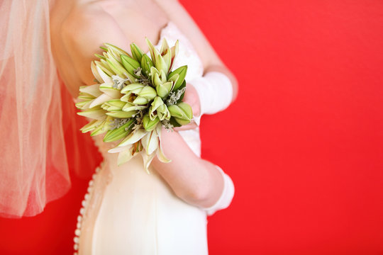 hands of young bride wearing white dress hold bouquet of lilies