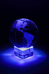 Small glass globe at glass stand is illuminated by blue light